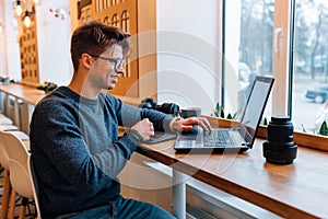 Cheerful man sitting at cafe and working on laptop