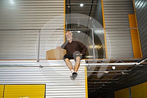 Cheerful man sitting on a container with a cardboard box
