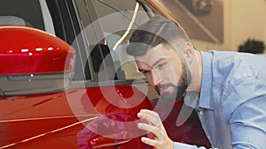 Cheerful man smiling to the camera while examining car at the dealership
