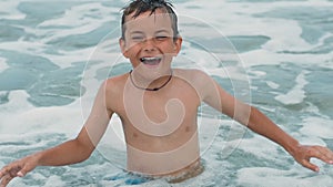 Cheerful man swashing in sea surf. Happy teenager wiping face at seaside.