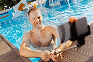 Cheerful man taking a selfie with a monopod in pool
