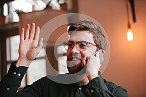 Cheerful man talking by phone and waving look aside.