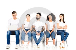 cheerful man using laptop while tired multiethnic group of people sitting on chairs isolated