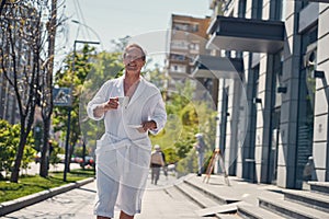 Cheerful man in white bathrobe walking on the street