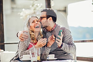 Cheerful man and woman dating and spending time together in cafe, using phone
