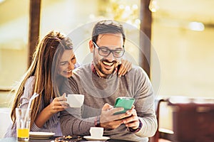 Cheerful man and woman dating and spending time together in cafe, using phone