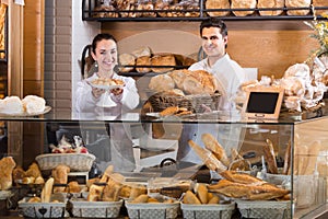 Cheerful man and woman selling pastry and loaves