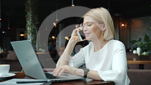 Cheerful manager talking on mobile phone and using laptop computer in cafe