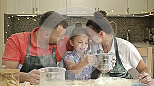 Cheerful married couple with a little daughter, cook some dough together, enjoy family activities.