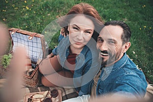 Cheerful married couple making selfie on meadow