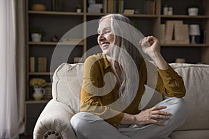 Cheerful mature 50s woman sitting on couch at home