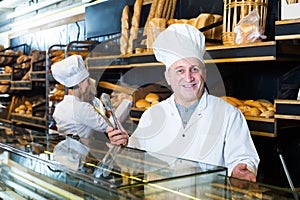 Cheerful mature bakers with fresh bread in bakery