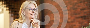 Cheerful mature businesswoman in glasses smiling away, using laptop and drinking coffee while working in the office