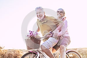 Cheerful mature couple of senior enjoy the outdoor leisure activity together riding a bike and laughing a lot - happy elderly