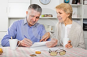 Cheerful mature couple at table attentively study documents