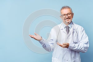 Cheerful mature doctor posing and smiling at camera, healthcare and medicine. Isolate on blue background.