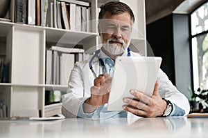 Cheerful mature doctor using digital tablet in clinic.