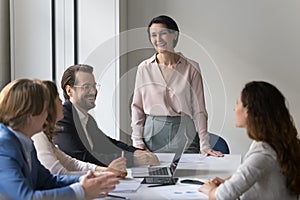 Cheerful mature female boss speaking to successful millennial professional team