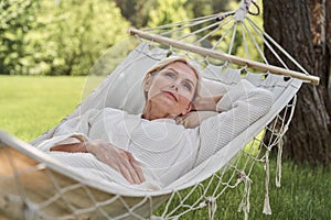 Cheerful mature female lying in hammock outdoors