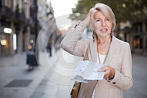 Cheerful mature female is walking with map and looking way