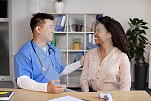 Cheerful mature korean doctor greets, congratulates with recovery black millennial lady patient in clinic