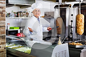 Cheerful mature man cook cutting kebab meat on kitchen