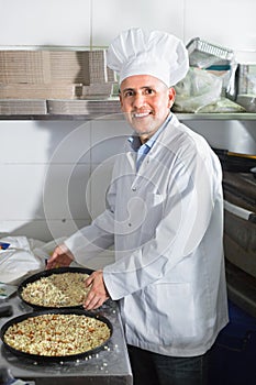Cheerful mature man cook making pizza in pan on kitchen