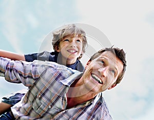 Cheerful mature man with his son on back flying against sky. Portrait of a cheerful mature man with his son on back