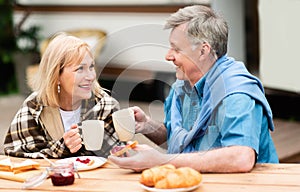Cheerful mature man and his wife enjoying morning coffee with jam toasts at campground