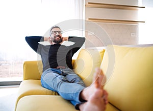 Cheerful mature man sitting on sofa in unfurnished house.
