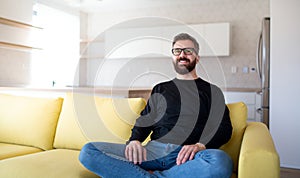 Cheerful mature man sitting on sofa in unfurnished house.