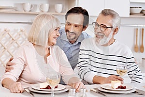 Cheerful mature son hugging elderly parents at home