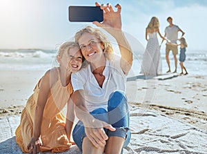 Cheerful mature woman and little girl taking a selfie while sitting on the beach. Happy little girl smiling while