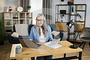 Cheerful mature woman presenting financial report to colleagues through video call on laptop.