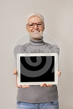 Cheerful mature woman showing blank screen on digital tablet