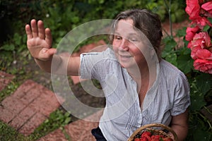 Cheerful mature woman sits in the garden and waving to friends photo