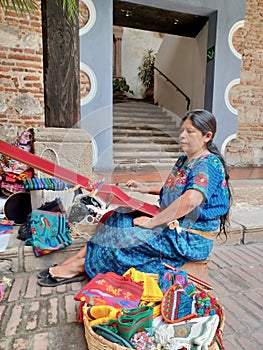 Cheerful mayan indian woman wearing a traditional huipil crafting handmade weavings in the city of Antigua in Guatemala.