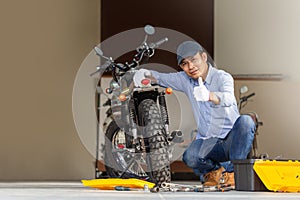 Cheerful mechanic repairing motorcycle in workshop garage, Smiling man fixing motorbike in repair shop, Man showing thumbs up,