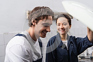 Cheerful mechanic standing near blurred colleague