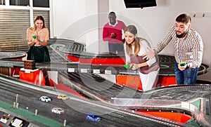 Cheerful men and women play together with slot car racing track