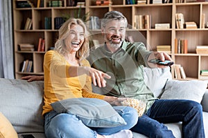 Cheerful middle aged couple having fun while watching tv at home together