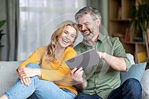 Cheerful Middle Aged Couple Relaxing With Digital Tablet At Home