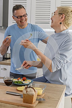 Cheerful middle-aged couple smiling while cooking lunch together at home - Healthfy retired lifestyle