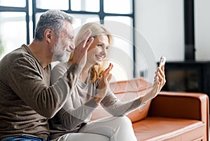 Cheerful middle-aged couple using smartphone for video connection