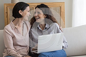 Cheerful middle aged mother and happy daughter woman using laptop