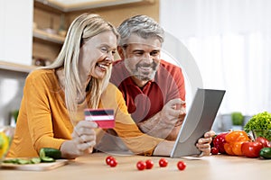 Cheerful middle aged spouses using digital tablet and credit card