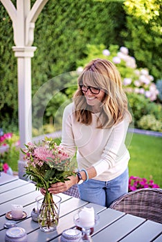 Cheerful middle aged woman arranging flowers on the table at home