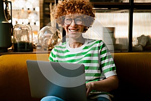 Cheerful middle-aged woman in eyeglasses using laptop while sitting in cafe