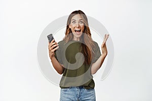 Cheerful middle aged woman holding mobile phone, looking at camera and screaming with rejoice, winning online smartphone