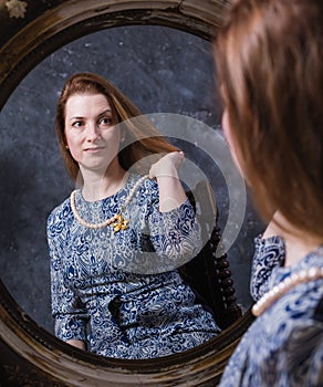 Cheerful middle aged woman looks in vintage style mirror